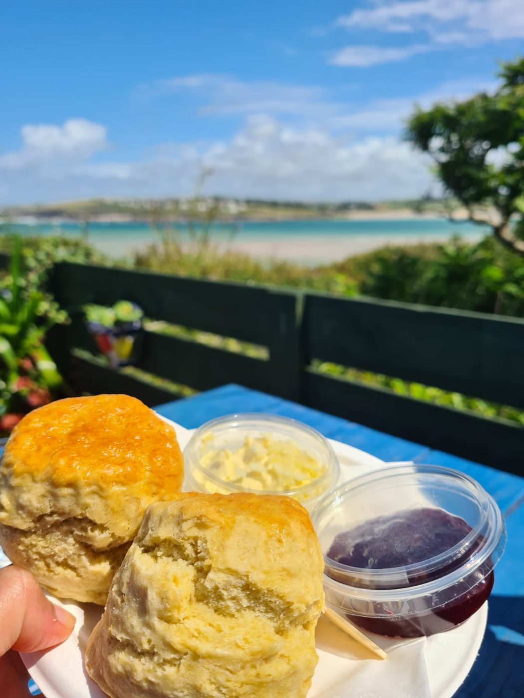Scones with jam and cream held up against the sea view